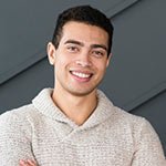 Junger Mann, der lächelt, trägt einen Pullover und steht mit verschränkten Armen.