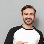 Junger Mann in einem schwarzen und weißen T-Shirt, zeigt auf sich und lächelt.